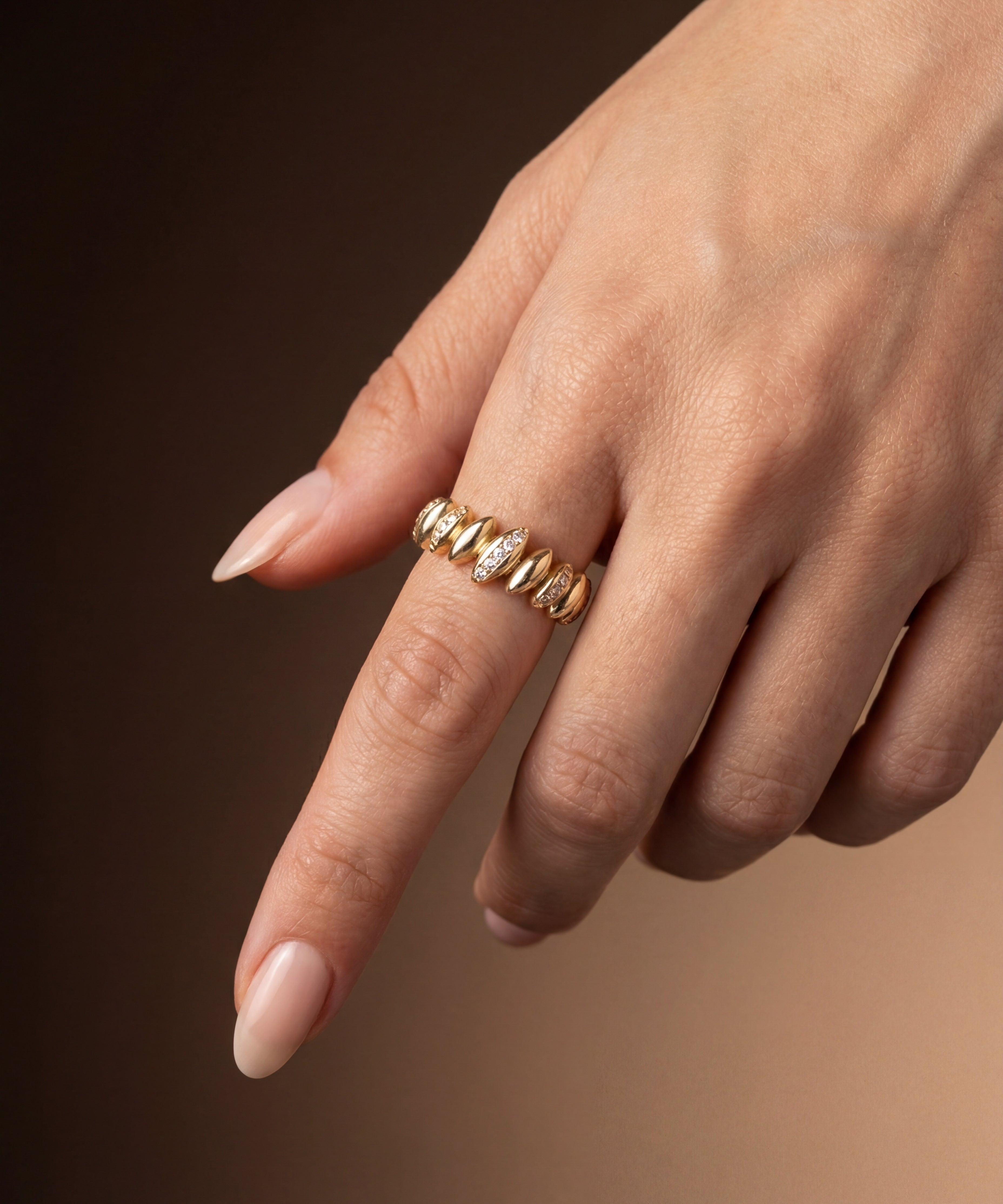 Gold ring with zircons on a finger against a brown background