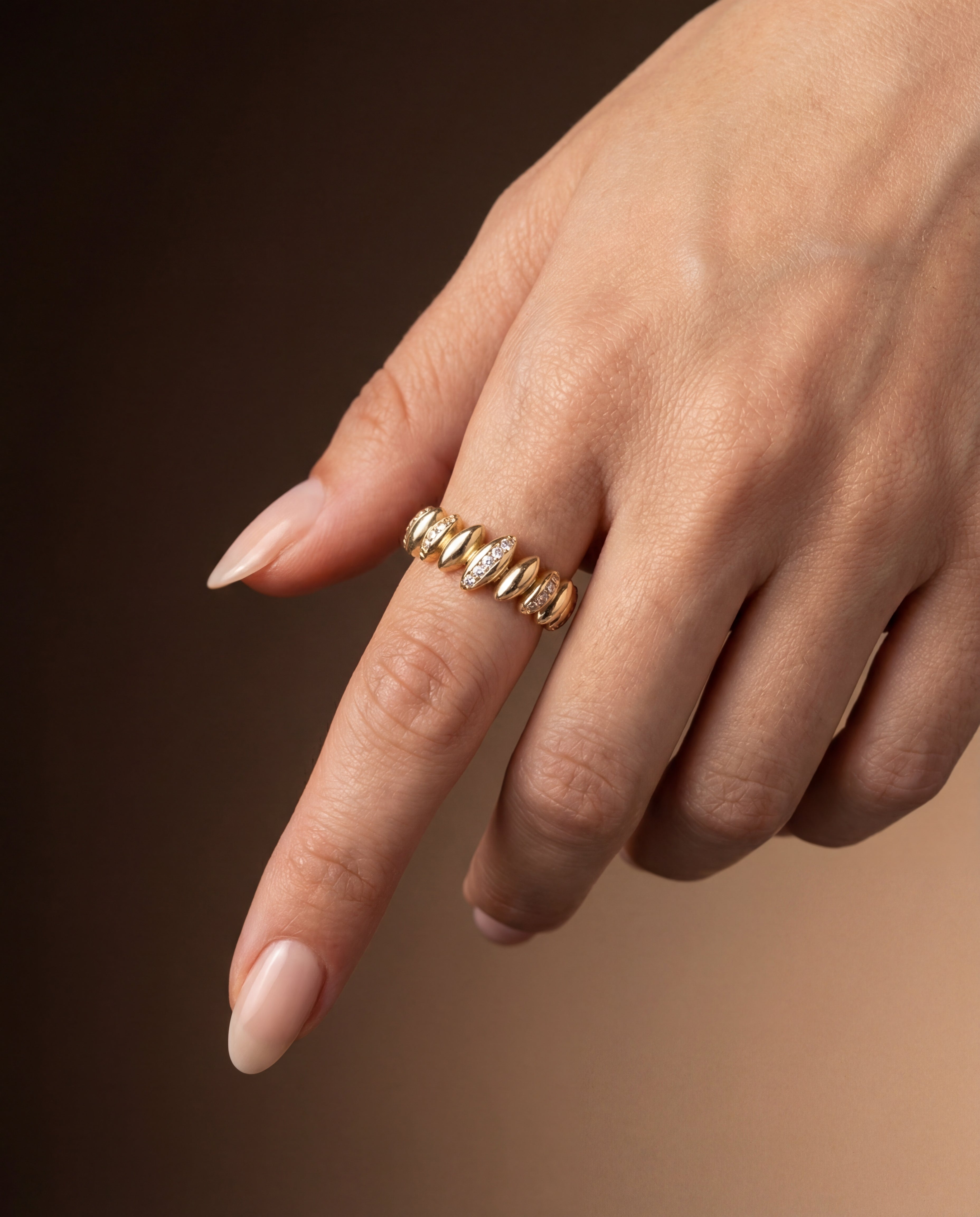 Gold ring with zircons on a finger against a brown background
