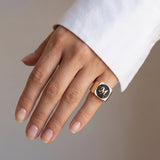 Hand wearing a gold signet ring with black diamonds on a neutral background