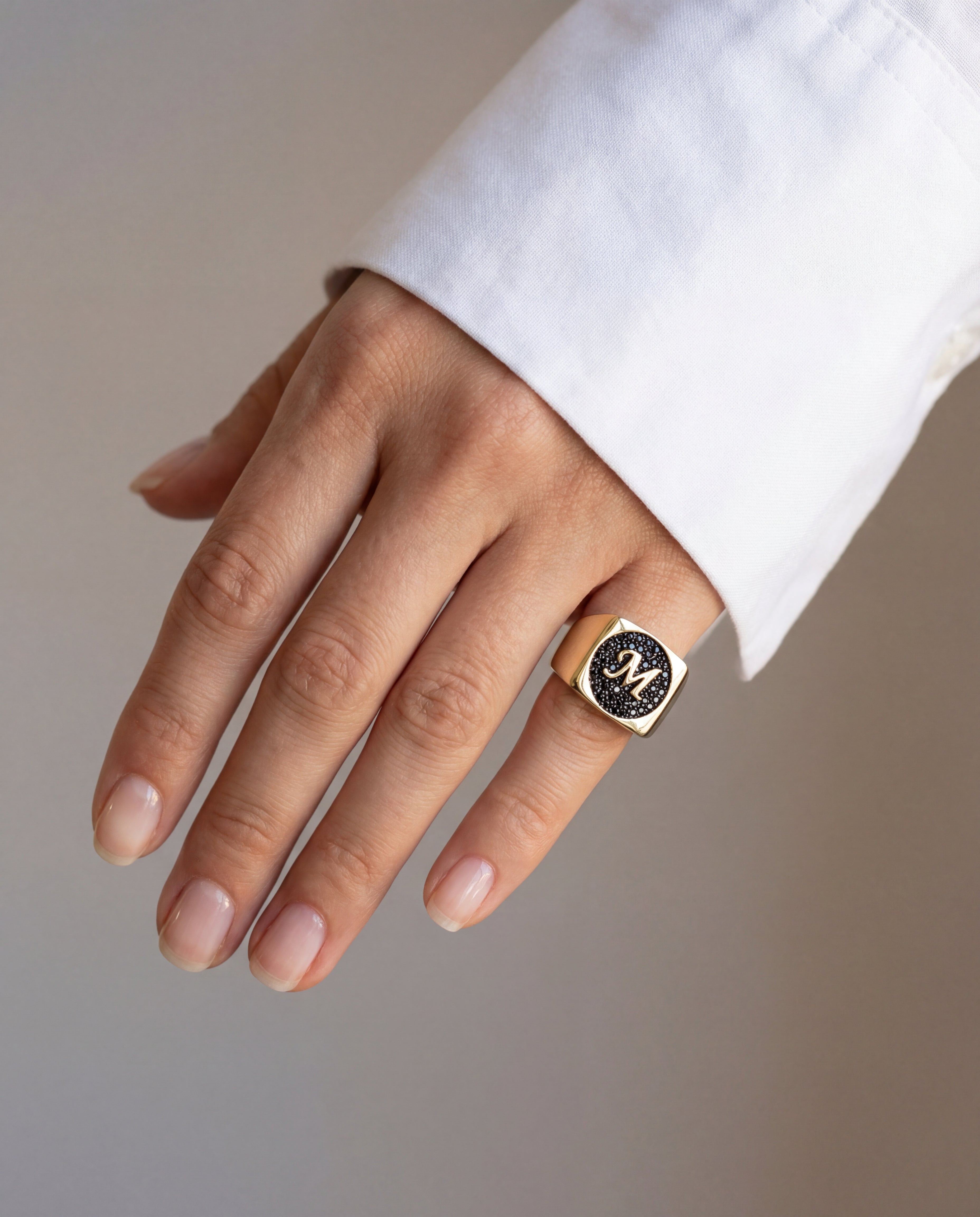 Hand wearing a gold signet ring with black diamonds on a neutral background