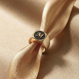 Gold ring with black diamonds with a monogram on a beige satin ribbon