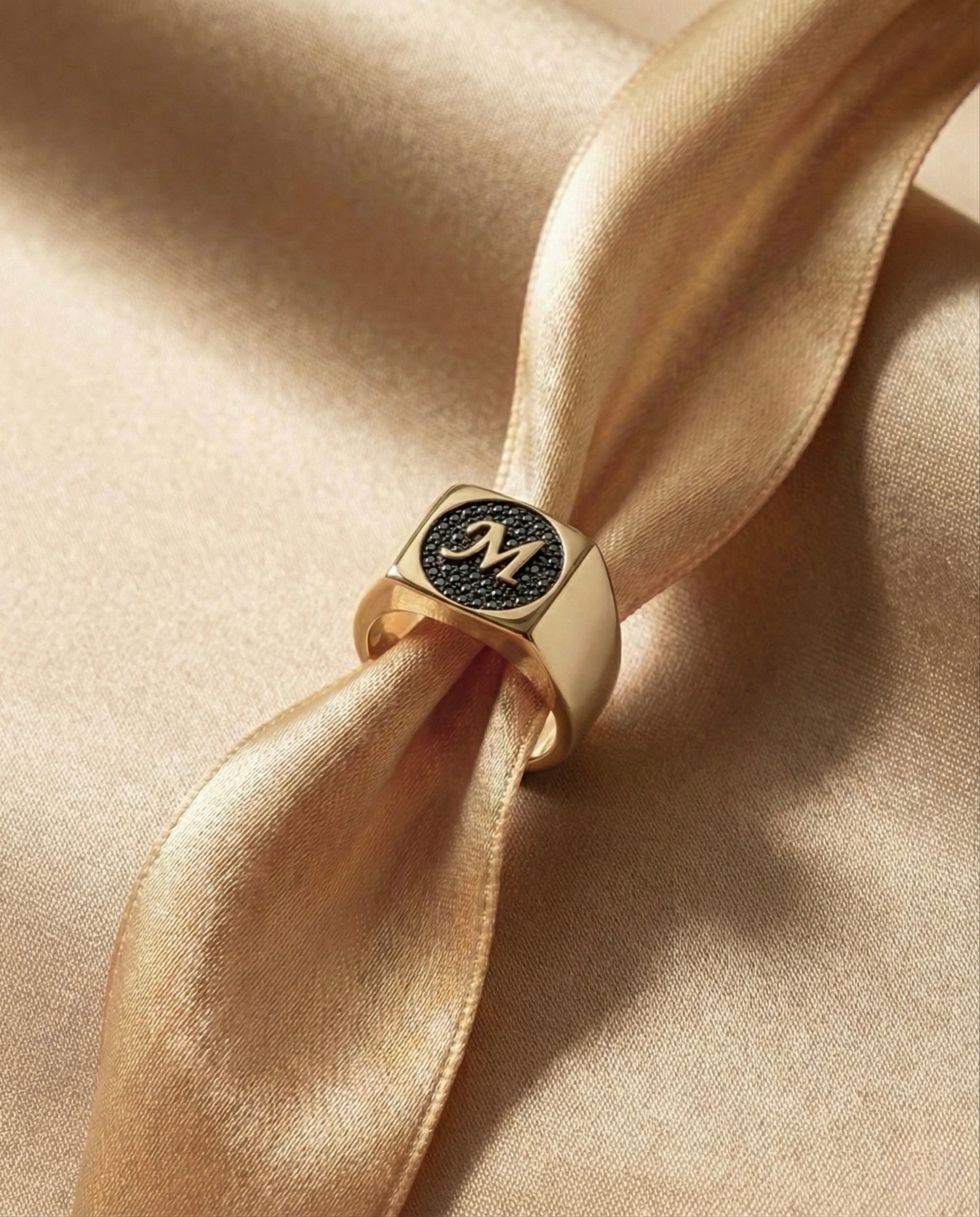 Gold ring with black diamonds with a monogram on a beige satin ribbon