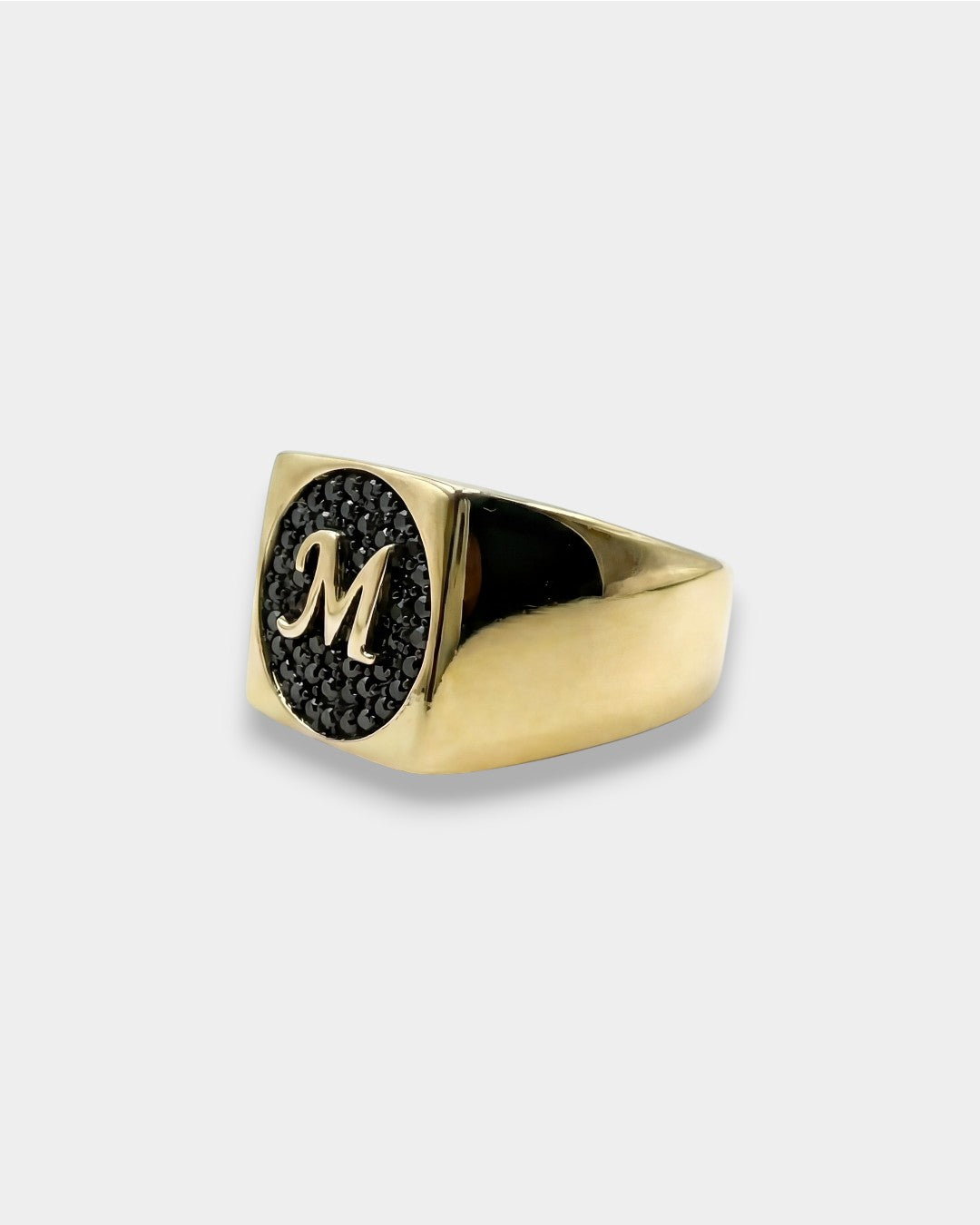 Gold ring with black gemstone and 'M' engraving on a white background