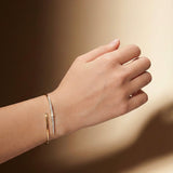 Hand wearing a gold bracelet on a warm-toned background