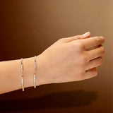 Hand wearing two white gold bracelets with zircons on a brown background