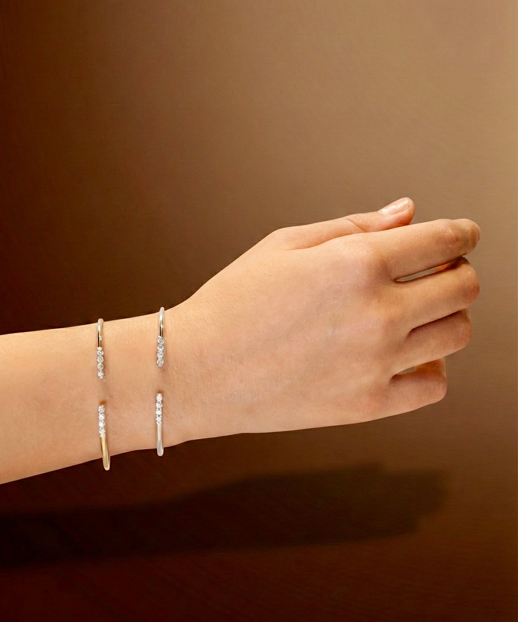 Hand wearing two white gold bracelets with zircons on a brown background