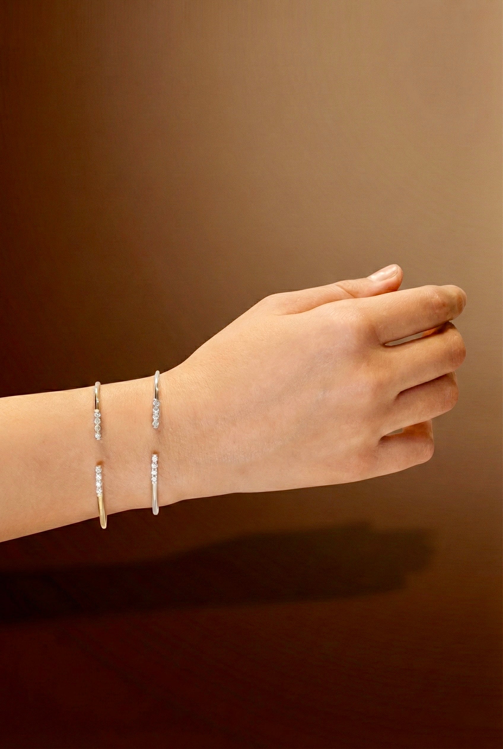 Hand wearing two white gold bracelets with zircons on a brown background