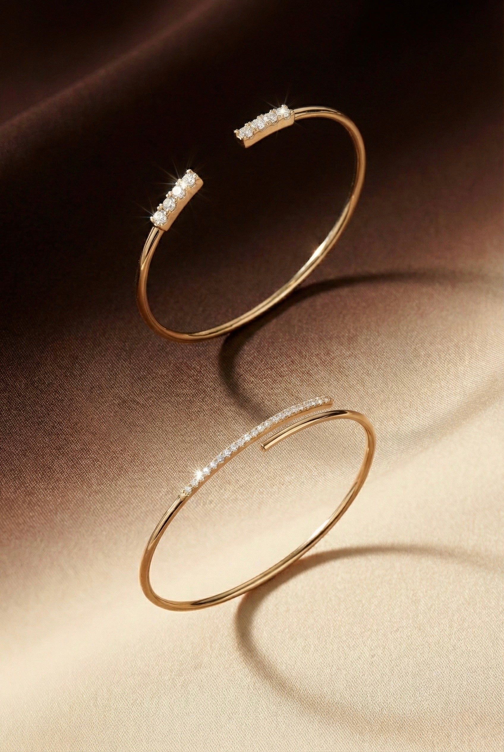 Two gold bangles with embedded stones on a brown surface