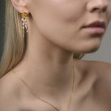 Close-up of a woman wearing a gold necklace and earrings against a neutral background
