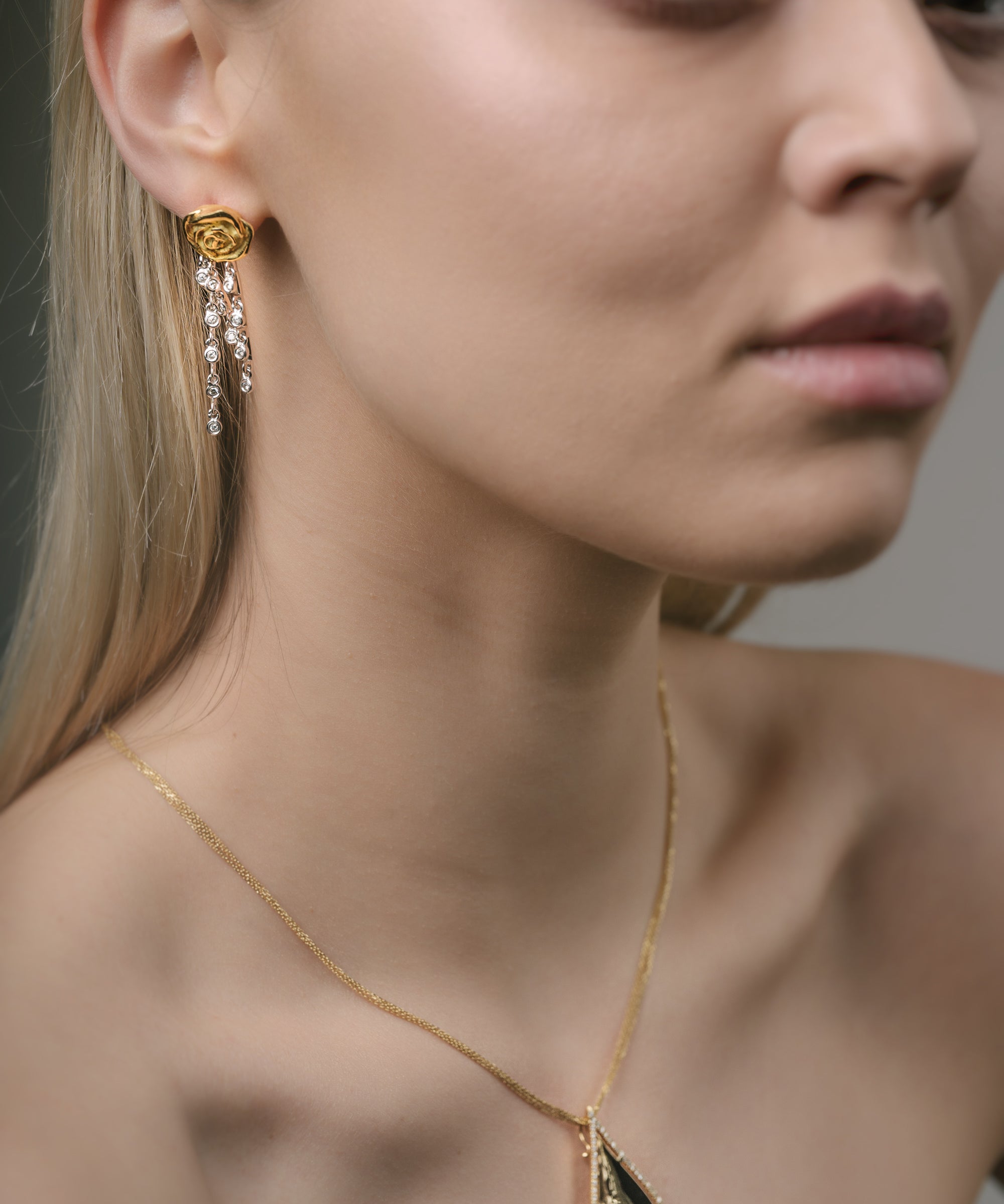 Close-up of a woman wearing a gold necklace and earrings against a neutral background