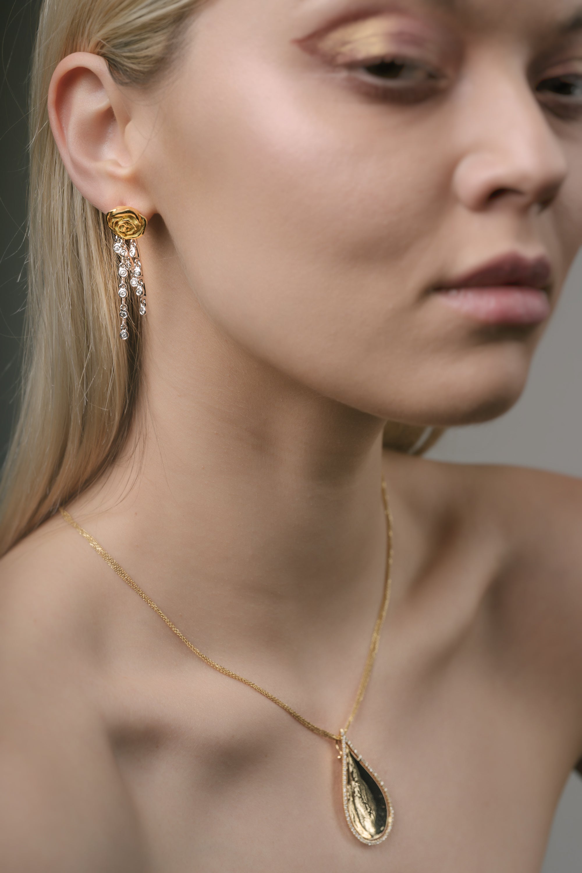 Close-up of a woman wearing a gold necklace and earrings against a neutral background