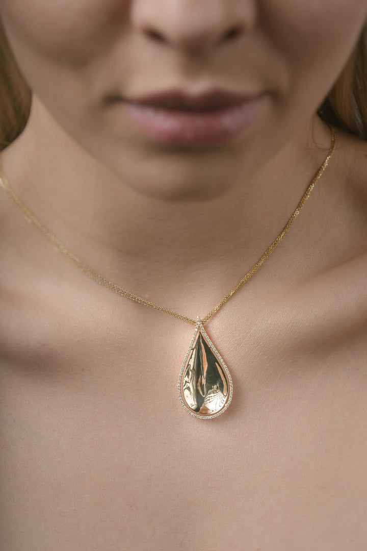Gold teardrop necklace on a person's neck with a blurred background