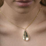Gold teardrop necklace on a person's neck with a blurred background