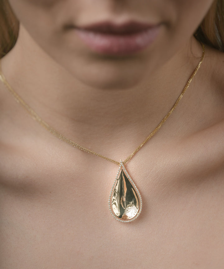 Gold teardrop necklace on a person's neck with a blurred background