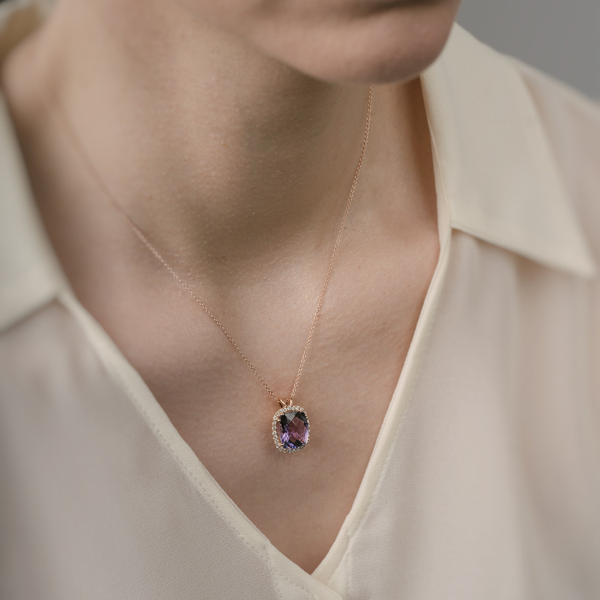 Necklace with a purple amethyst pendant worn by a person in a beige shirt.