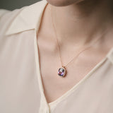 Necklace with a purple amethyst pendant worn by a person, focusing on the jewelry against a neutral background.