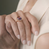 Close-up of a hand wearing a rose gold ring with a purple amethyst on a neutral background