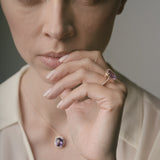 Woman wearing a ring with a purple amethyst against a neutral background