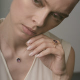 A woman wearing a necklace with a purple amethyst and holding a ring.