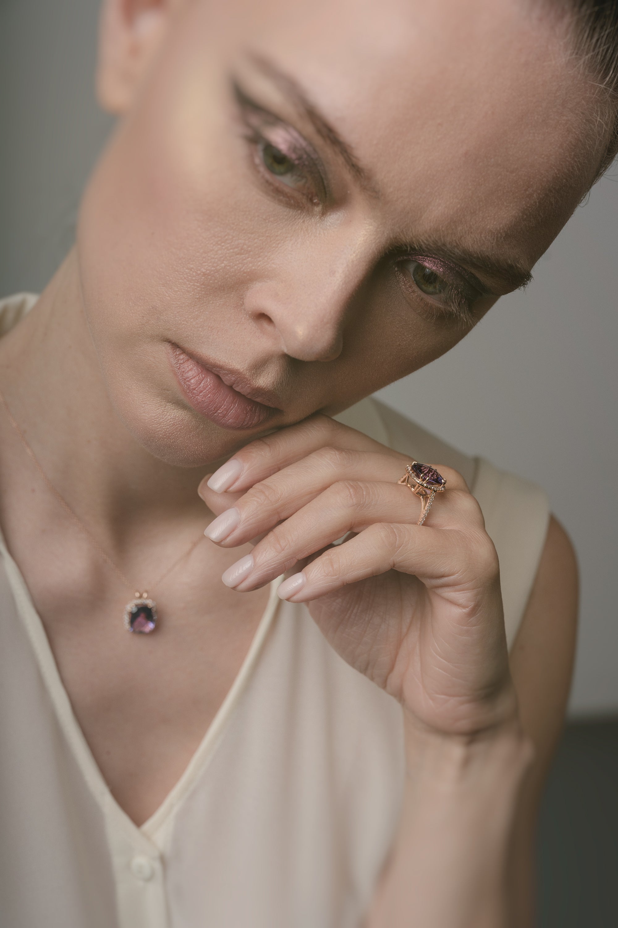 A woman wearing a necklace with a purple amethyst and holding a ring.