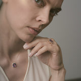 Woman wearing a necklace and ring with a purple amethyst against a neutral background