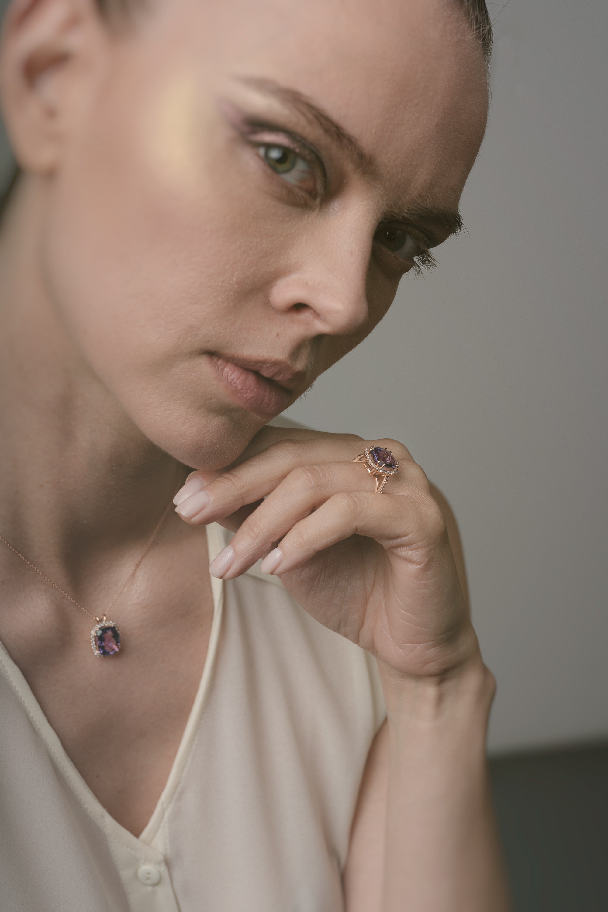 Woman wearing a necklace and ring with a purple amethyst against a neutral background