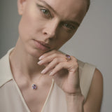Woman wearing a matching ring and necklace with purple amethyst against a neutral background