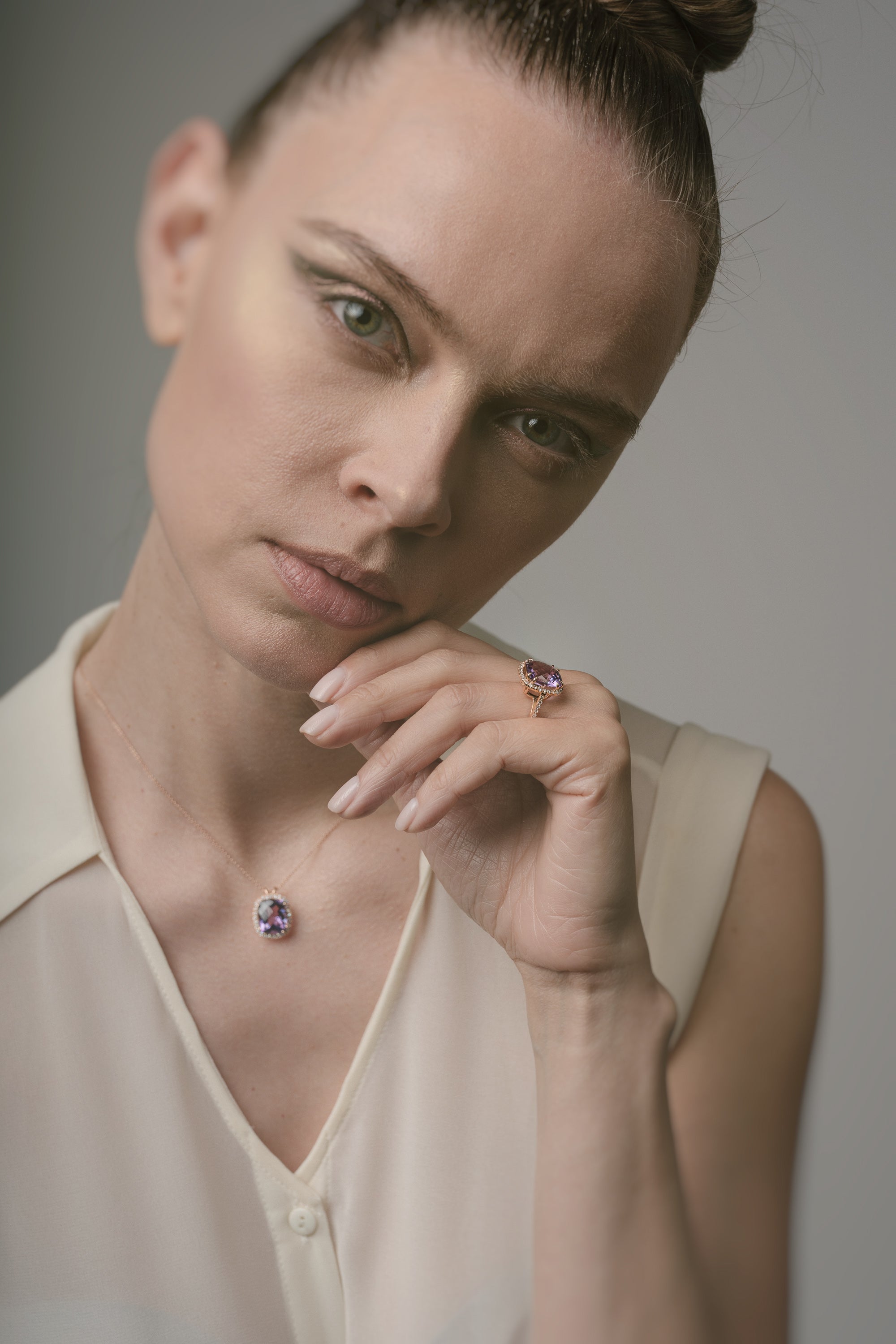 Woman wearing a matching ring and necklace with purple amethyst against a neutral background