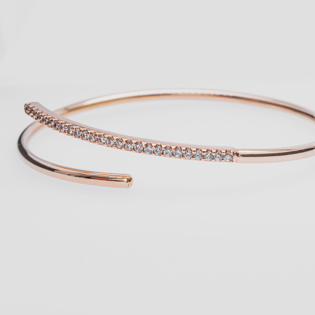 Rose gold bangle with diamond accents on a light gray background