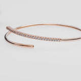 Rose gold bangle with diamond accents on a light gray background