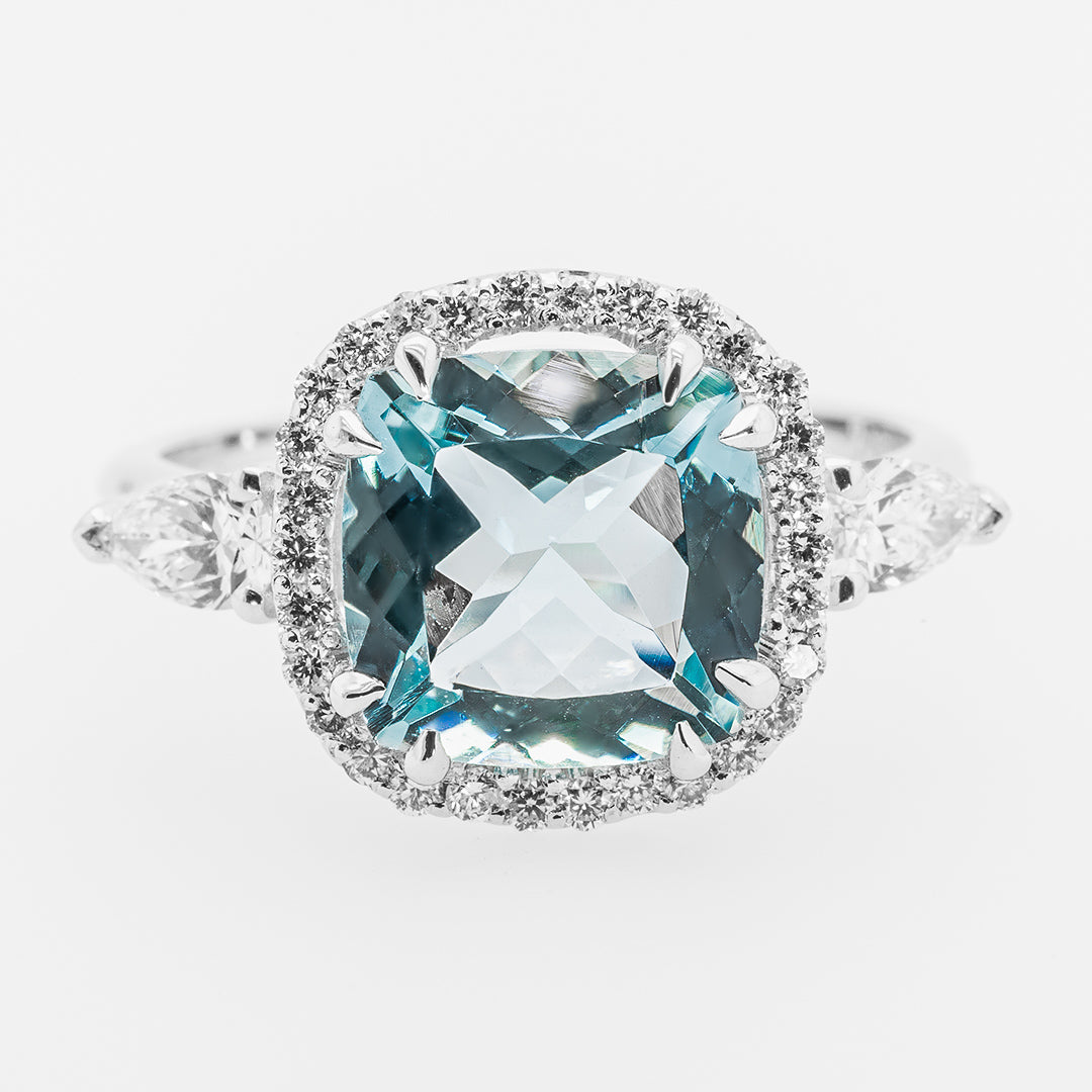 Ring with a large blue aquamarine gemstone and diamond-studded halo on a white background