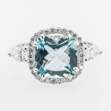 Ring with a large blue aquamarine gemstone and diamond-studded halo on a white background