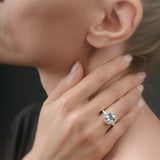 Close-up of a hand wearing a ring with a aquamarine gemstone, touching the neck.