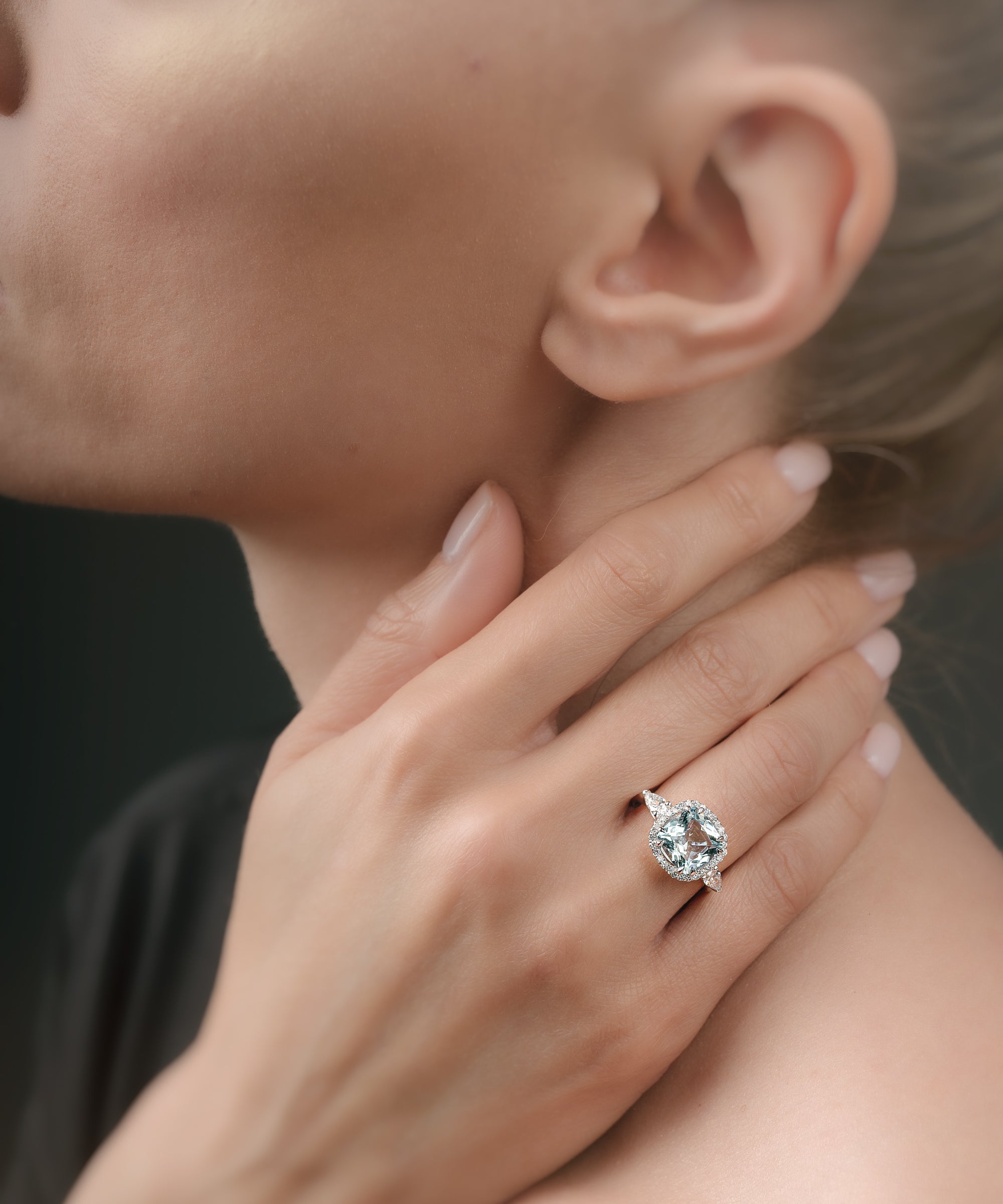 Close-up of a hand wearing a ring with a aquamarine gemstone, touching the neck.