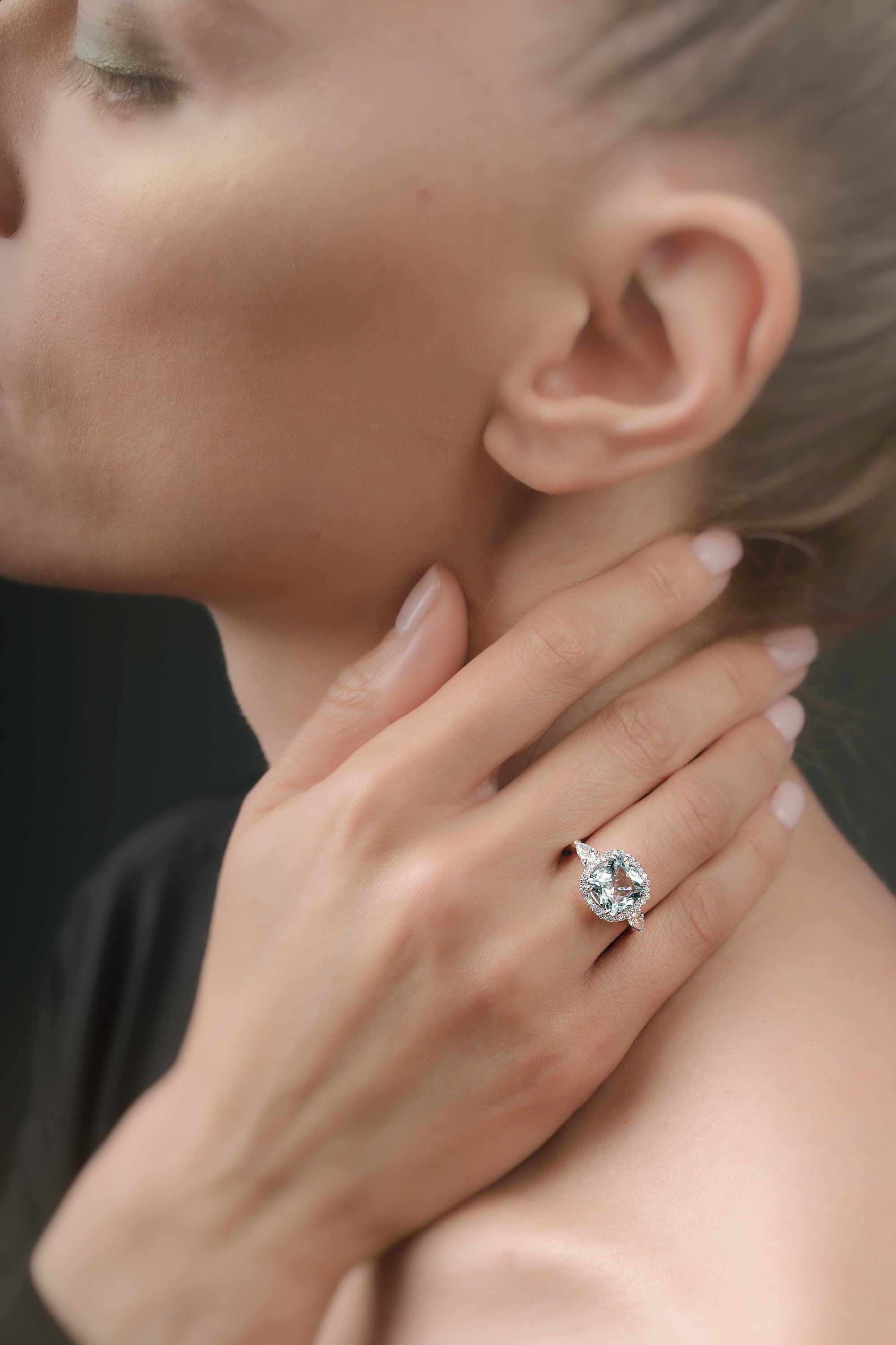 Close-up of a hand wearing a ring with a aquamarine gemstone, touching the neck.