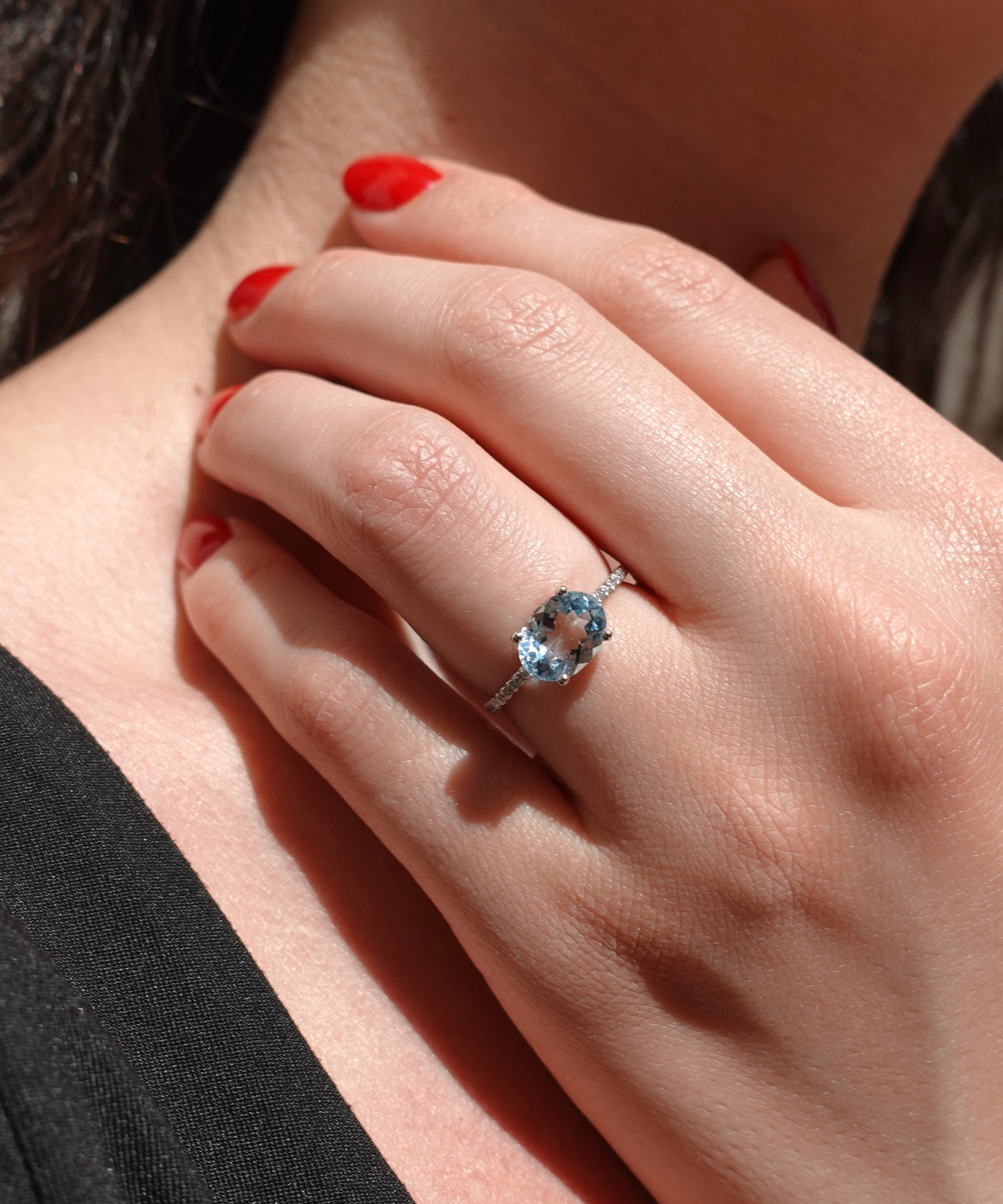 Close-up of a hand wearing a ring with a blue aquamarine gemstone, held against a blurred background.