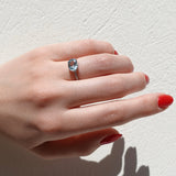 Hand wearing a ring with a clear aquamarine gemstone on a light background