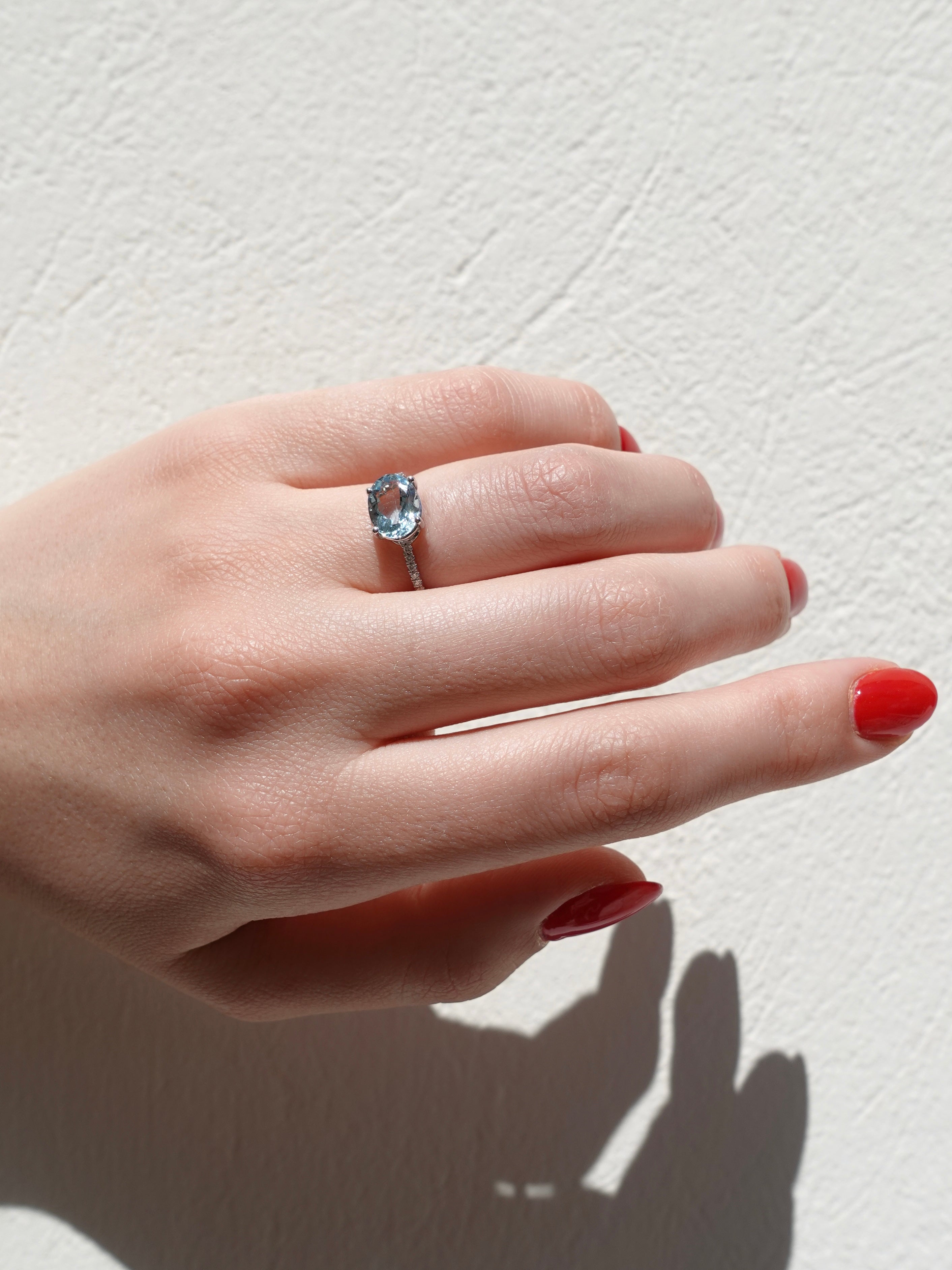Hand wearing a ring with a clear aquamarine gemstone on a light background