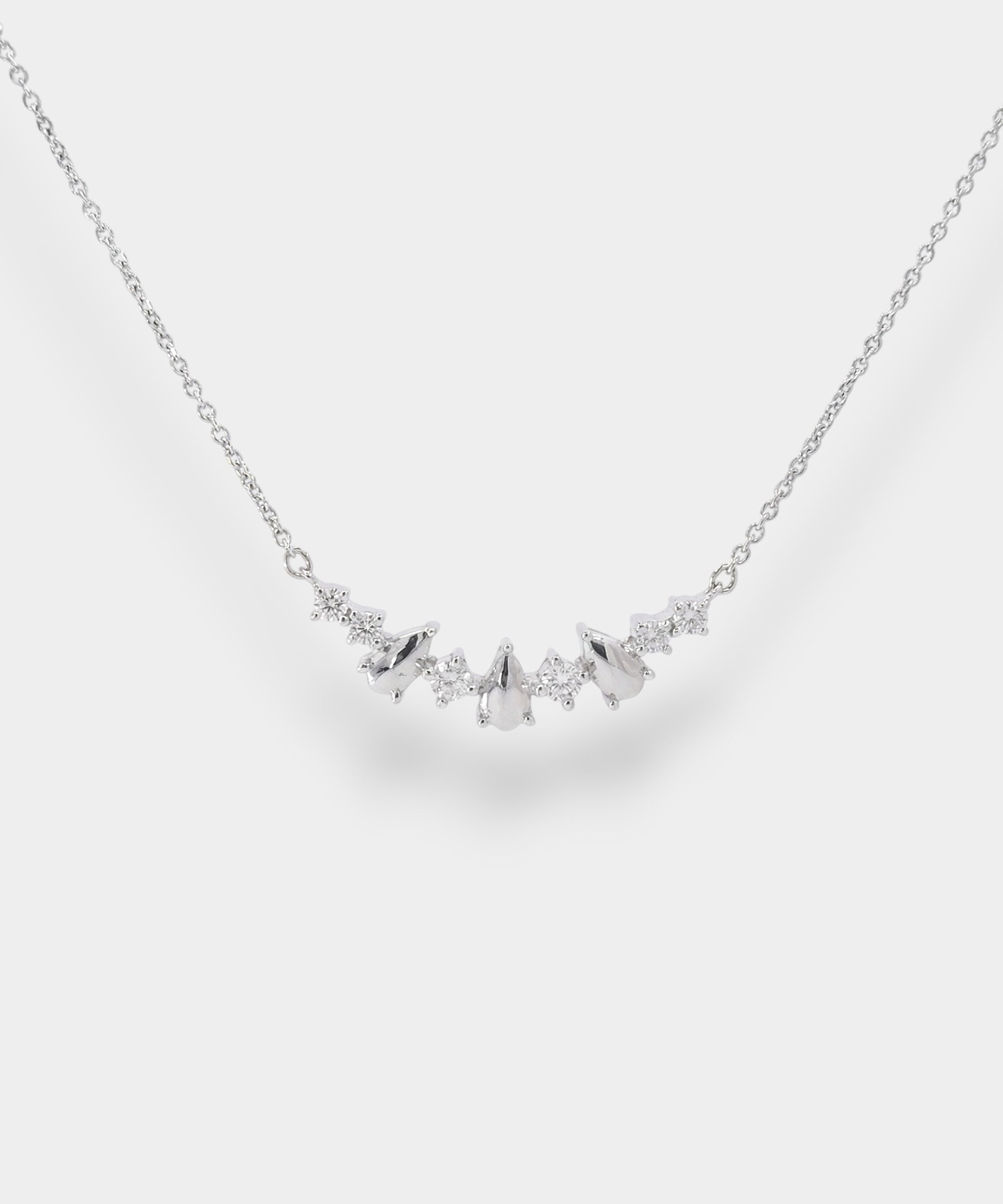 White gold necklace with small teardrop pendents and diamonds on a light gray background
