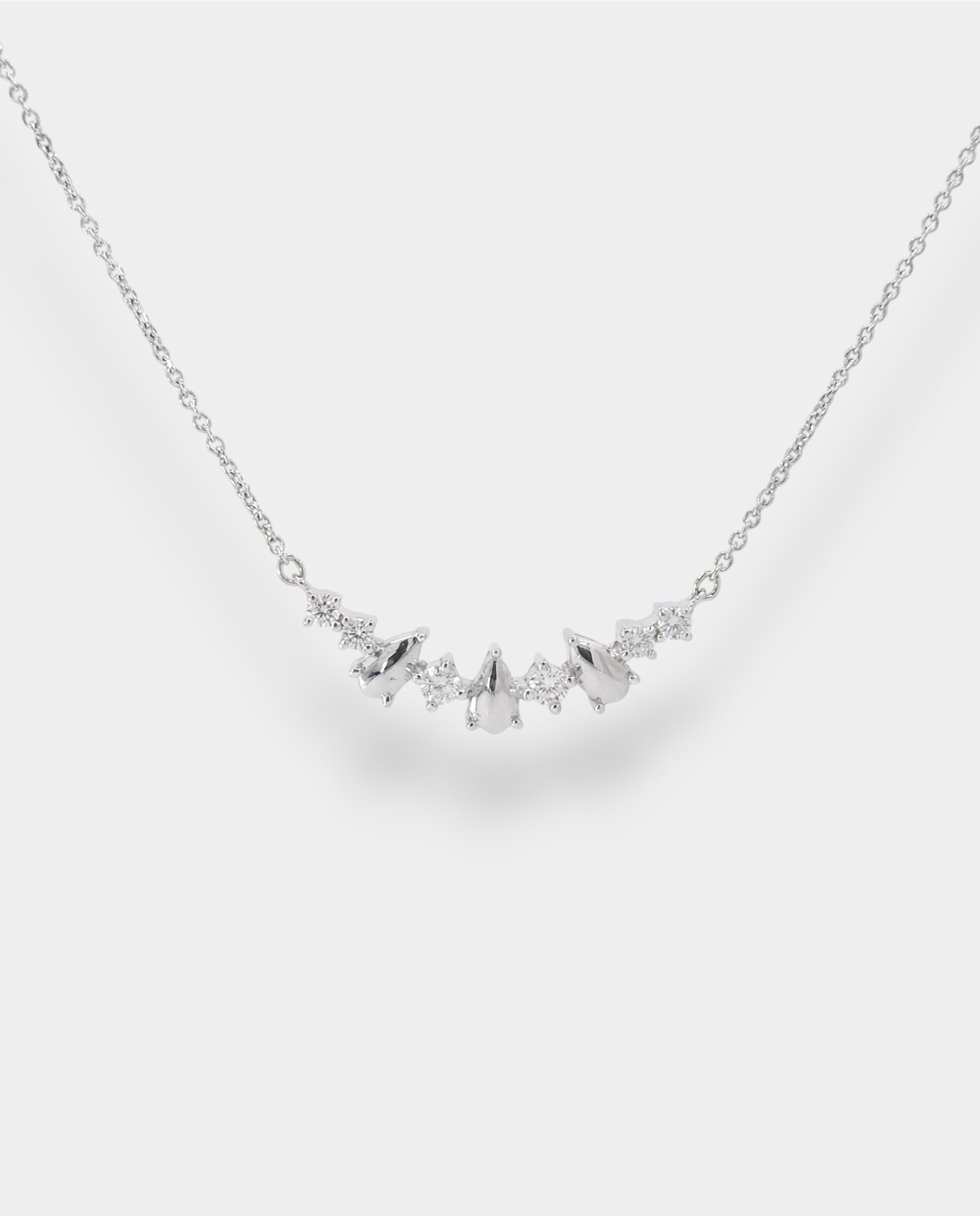 White gold necklace with small teardrop pendents and diamonds on a light gray background
