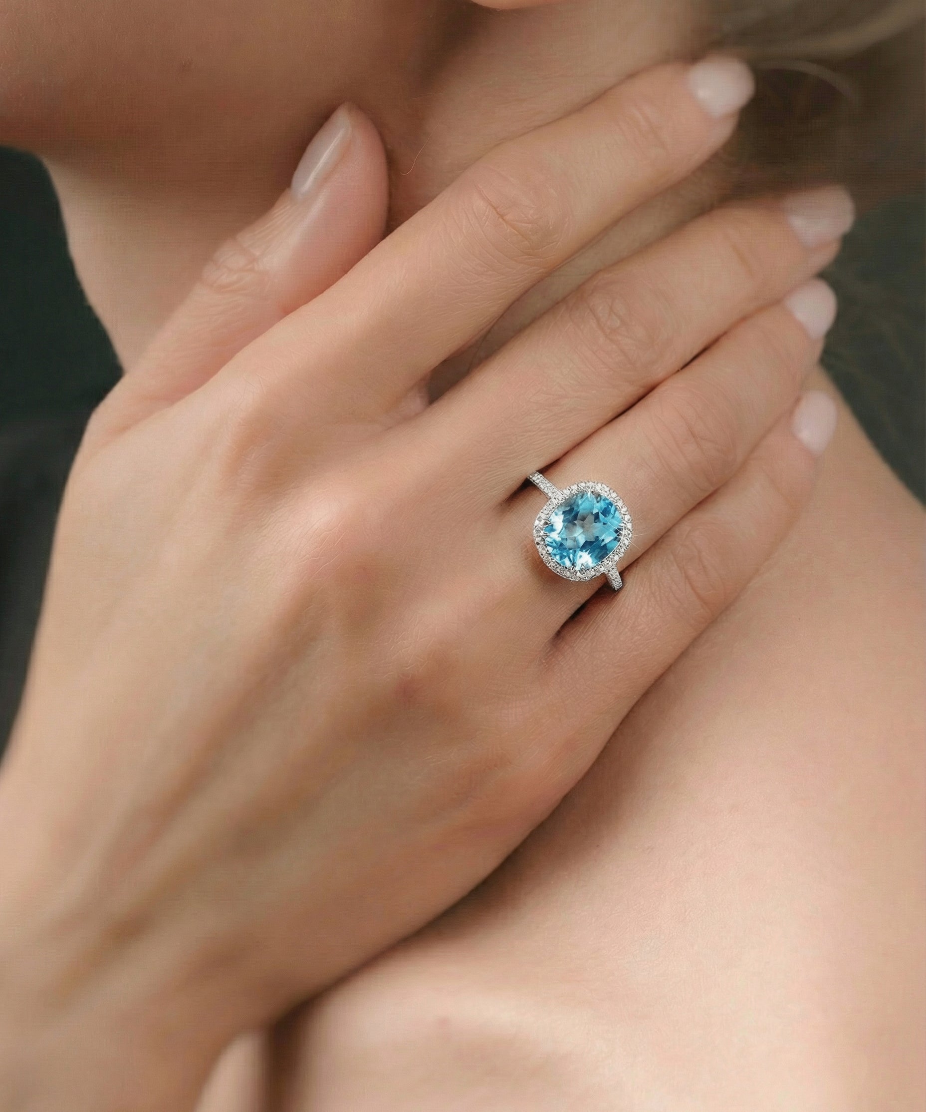 Close-up of a hand wearing a ring with a blue topaz, held near the face.