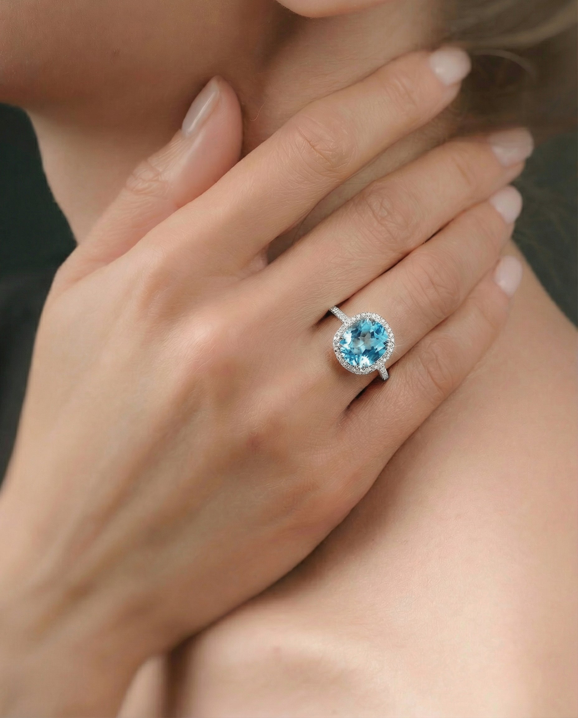 Close-up of a hand wearing a ring with a blue topaz, held near the face.