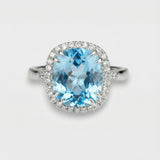 Ring with a blue topaz and diamond-studded halo on a light gray background