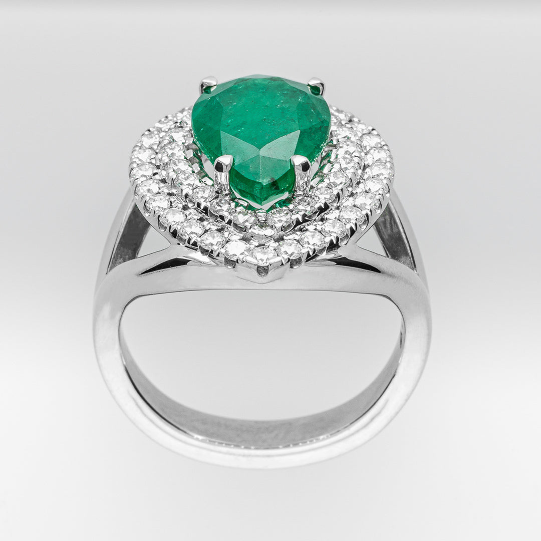 White gold ring with a green emerald gemstone and diamond halo on a light gray background