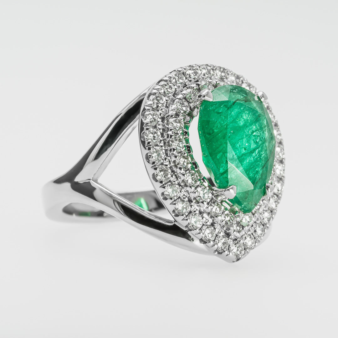 White gold ring with an emerald gemstone and diamond accents on a light gray background