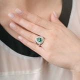 Hand wearing a ring with an emerald stone against a neutral background