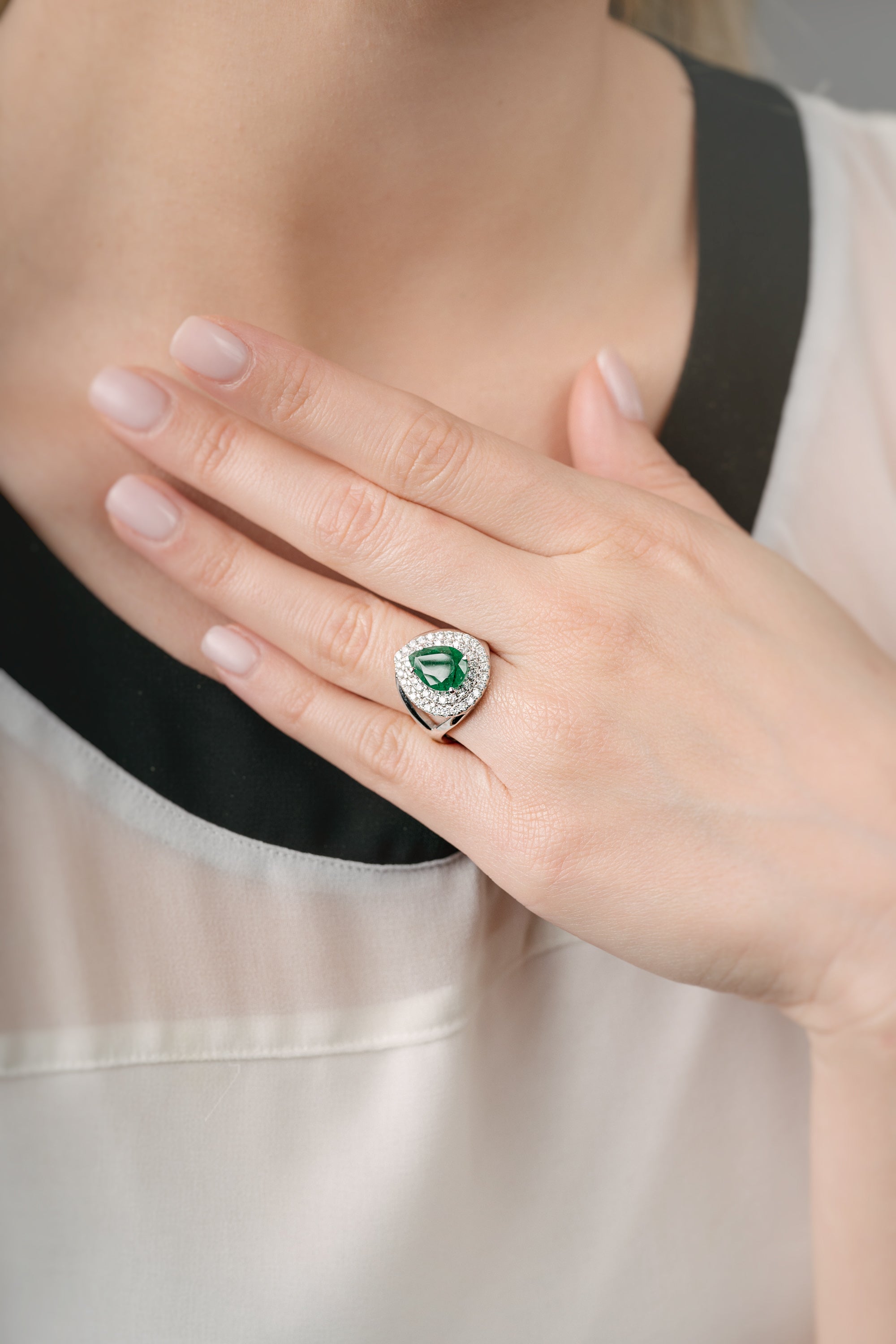 Hand wearing a ring with an emerald stone against a neutral background