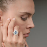 Woman wearing a ring with a blue gemstone on a gray background