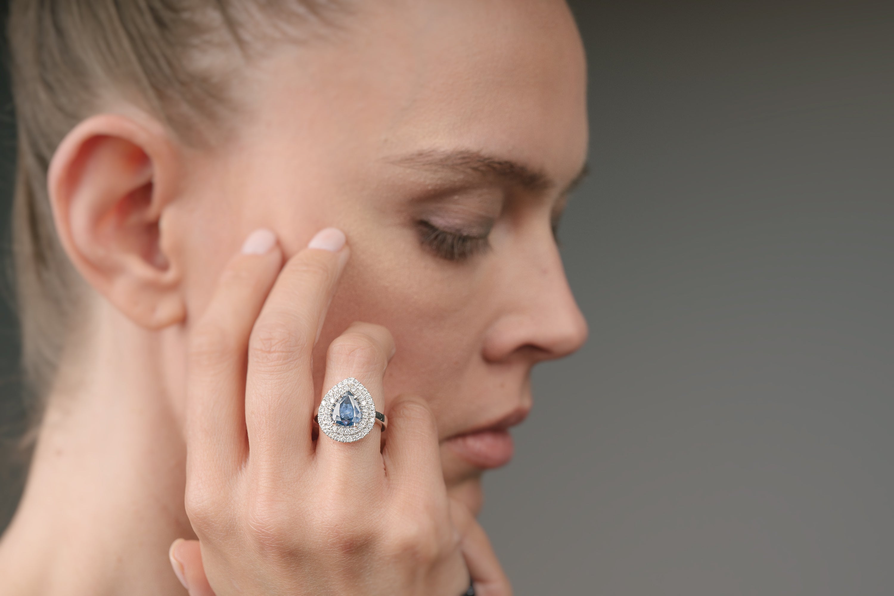 Woman wearing a ring with a blue gemstone on a gray background