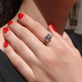 Close-up of a hand wearing a ring with a blue aquamarine gemstone, against a blurred background.
